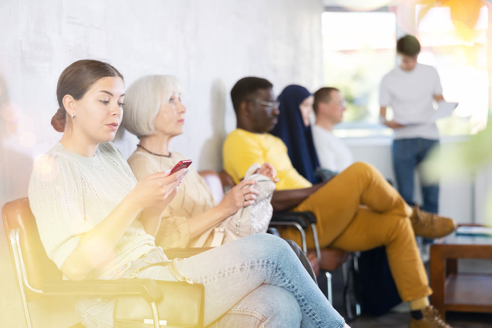 Positive young girl sitting with smartphone in lobby of medical clinic