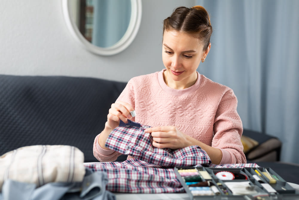 Young woman sewing on button at home