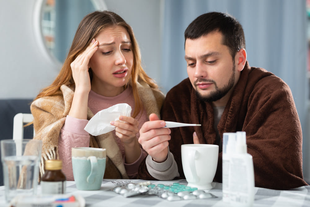 Woman and man wrapped in plaids having symptoms of cold at home