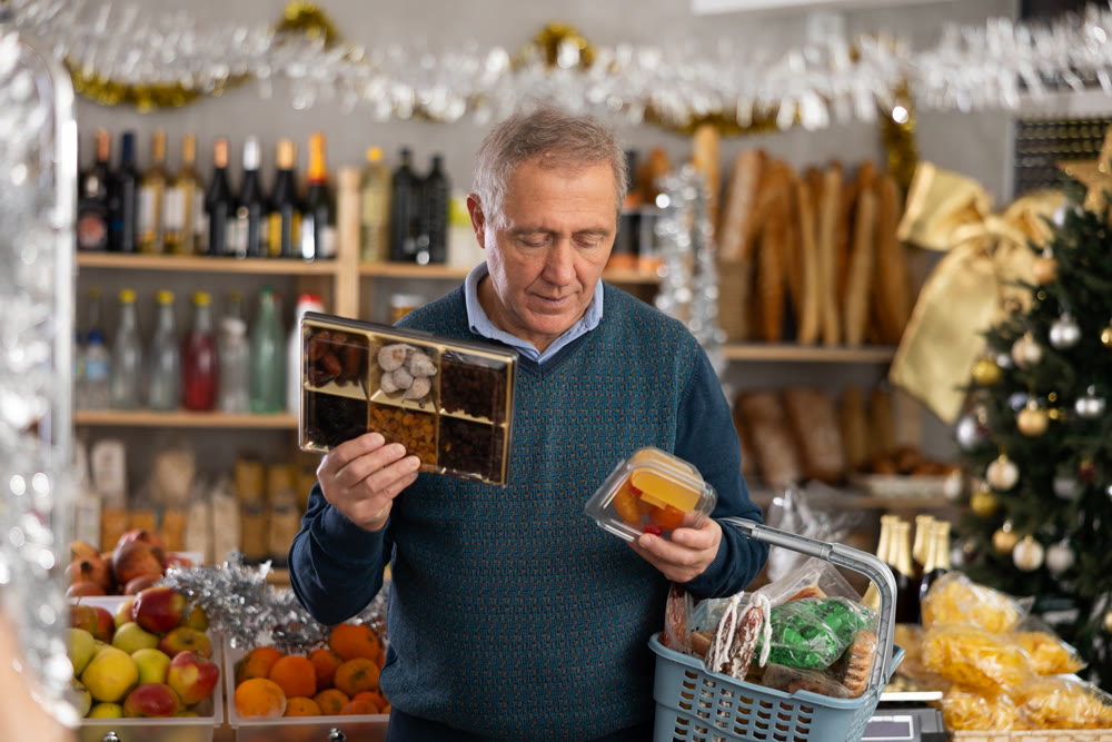 Man prepares to celebrate Christmas by choosing sweet dried fruits in produce section of supermarket