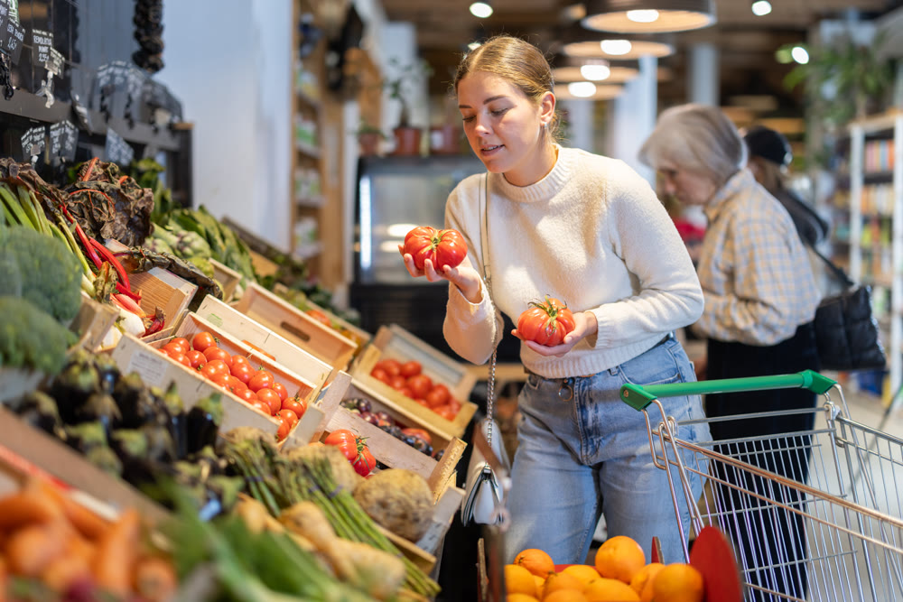 In cozy self-service store, girl customer takes tomatoes out of box