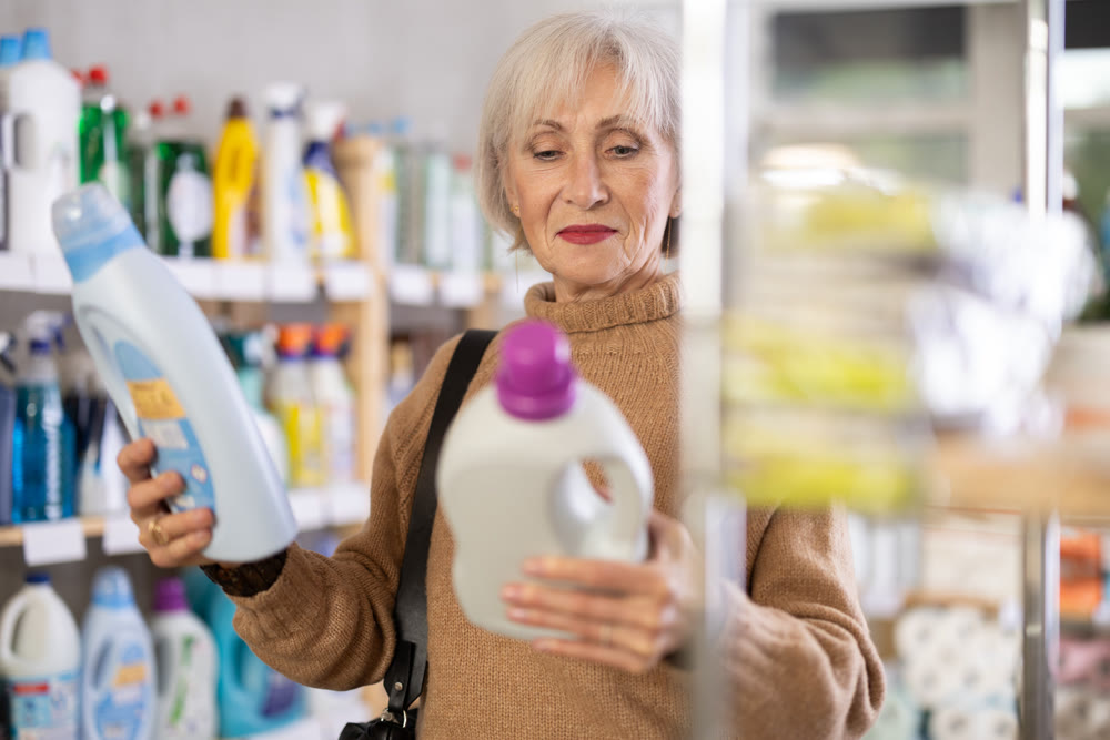 Mature positive woman consumer with household chemical products for washing indoors