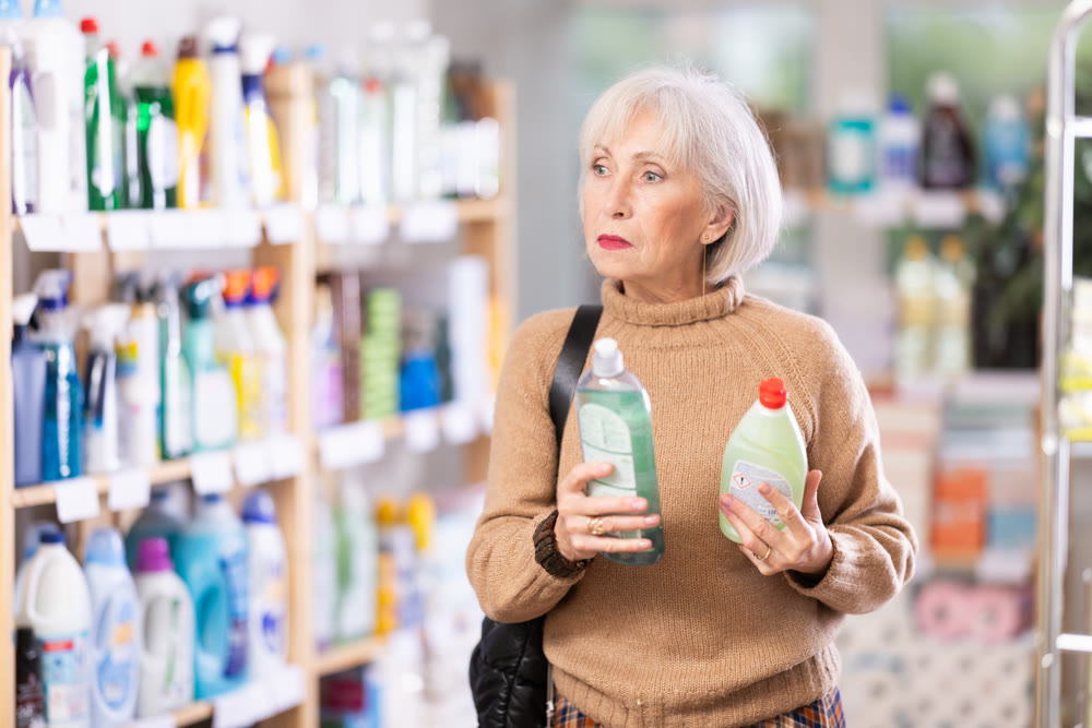 Elderly female customer diligently picking out dishwashing liquid