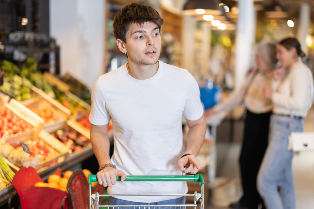 Young guy with shopping cart chooses groceries