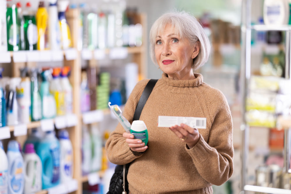 Portrait of an elderly woman choosing mouthwash and toothbrush in supermarket