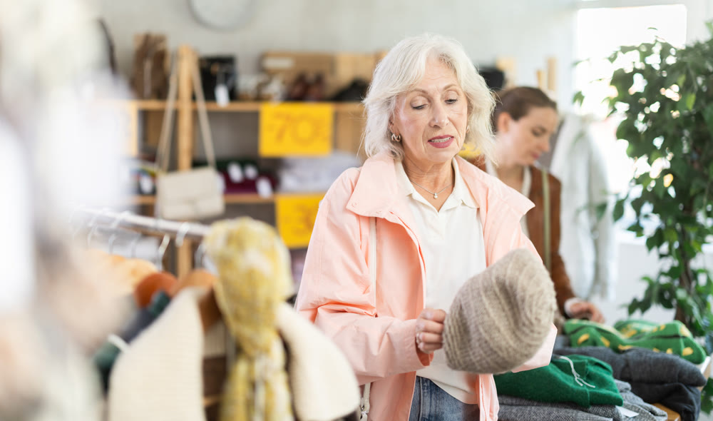 Mature woman choosing a hat for the winter in the store against the background of the buyer