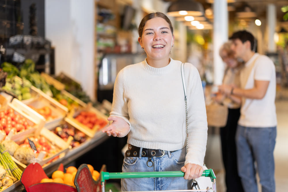 Young woman with shopping cart chooses groceries