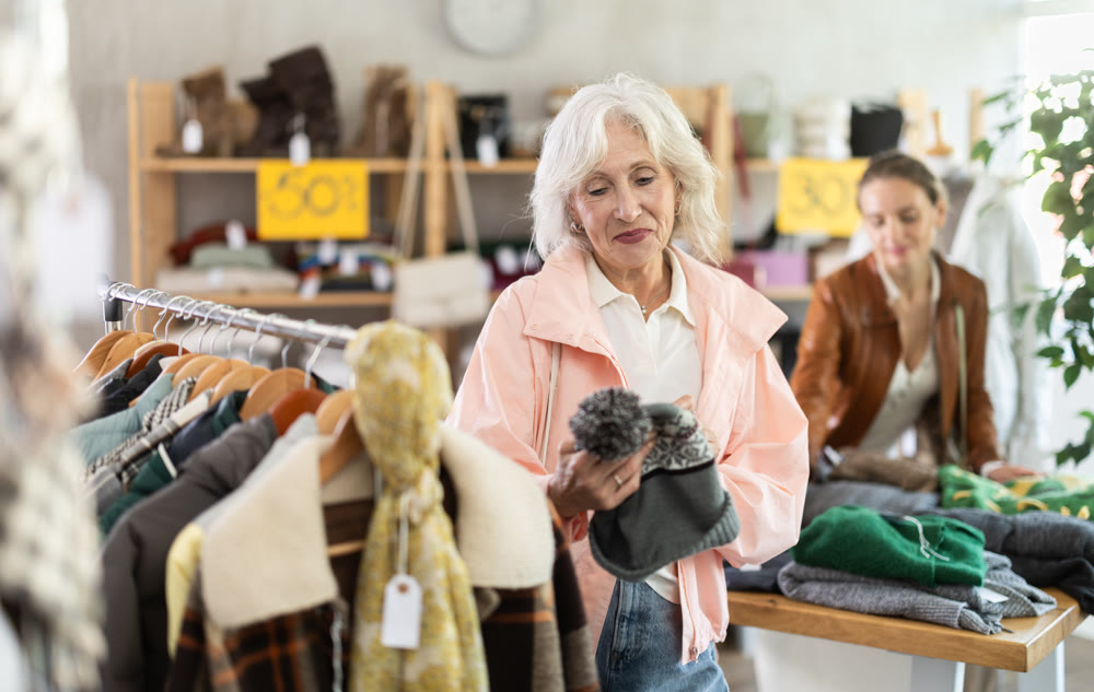 Senior woman customer examine and choose hat. Other buyer in background, crowded shop