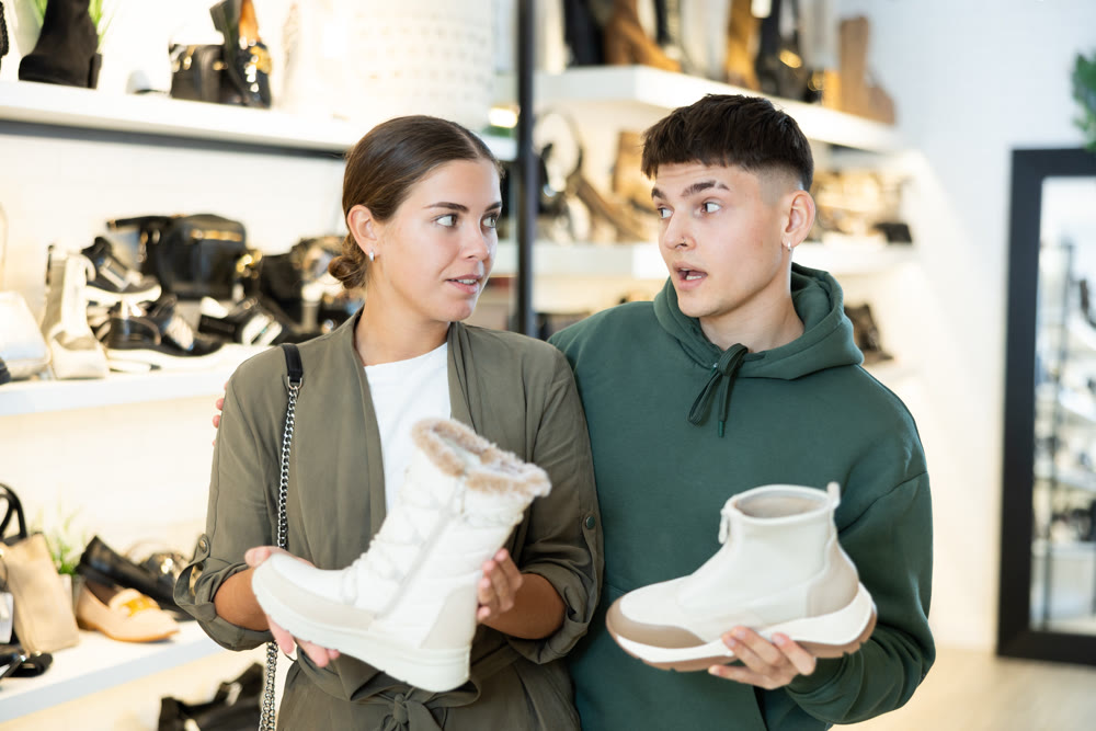 Young couple discussing choice of winter womens boots in shoe store