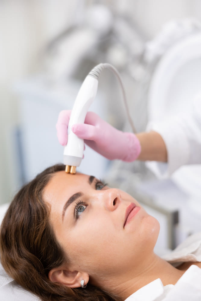 Faceless dermatologist performing cosmetology procedure for young woman, RF lifting and vacuum massage for facial skin therapy in clinic