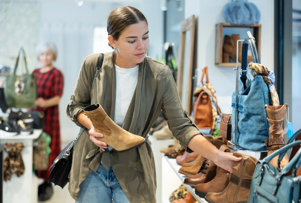 Girl buyer looks at footwear from new collection and picks up new pair of boots for winter.