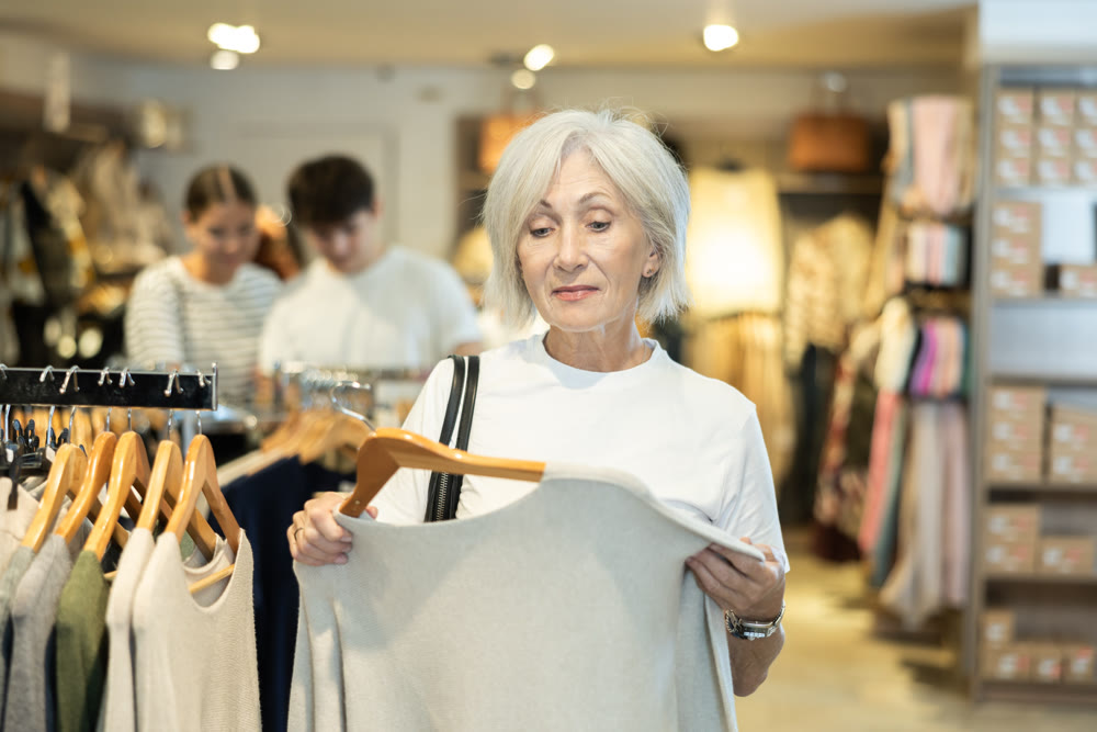 elderly lady carefully examines selection of sweaters