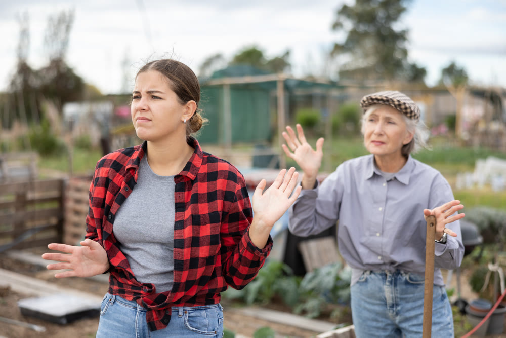 Two angry casual women neighbors of different ages arguing during the vegetable garden season on sunny day of spring