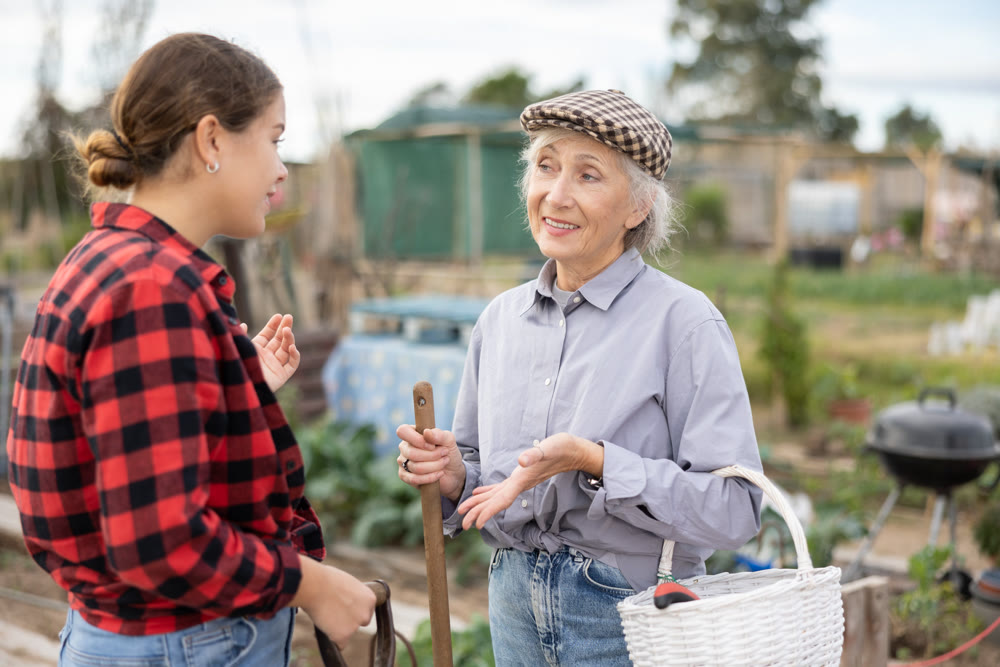 Two female gardeners talking near wooden fence in garden
