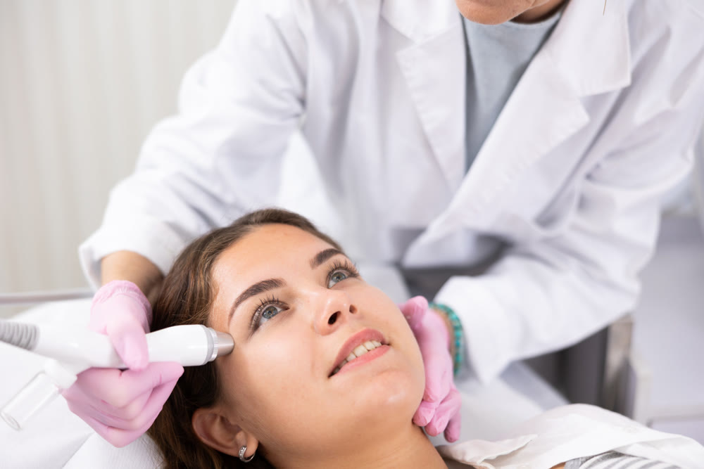 Elderly female beautician doing procedure of microneedling, mesotherapy for young woman in beauty salon indoors