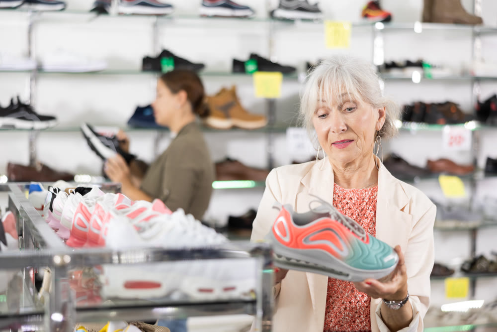 In multi-brand leather goods store,senior lady chooses modern comfortable running sneakers for fitness