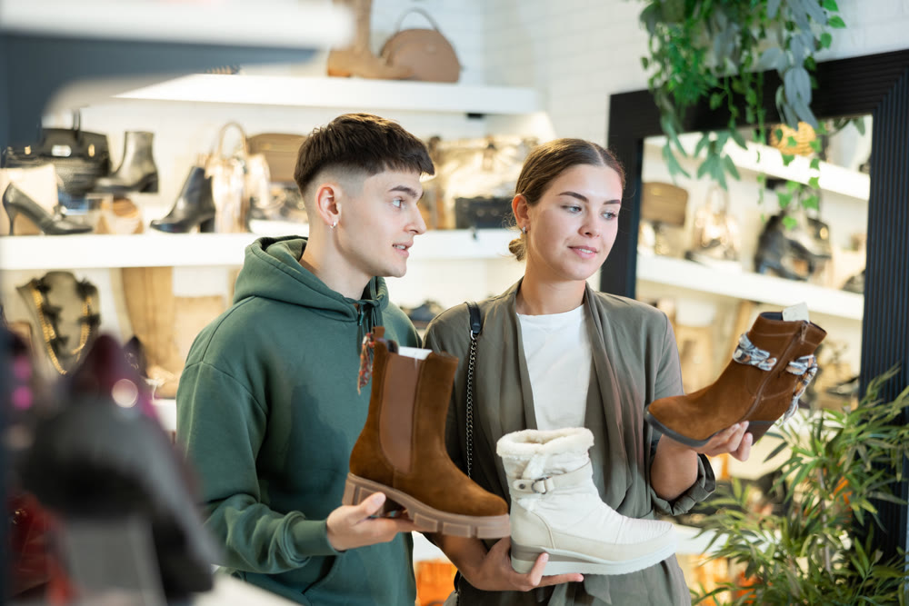 Young guy and girl choosing demi-season womens boots in shoe store