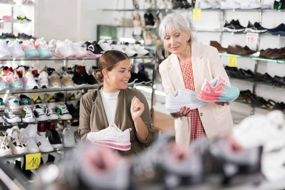 Elderly woman and young woman trying on sneakers in shoe store