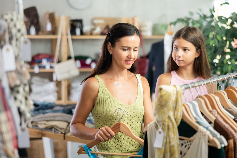 Near rack, daughter with mom buys something summer cloth, chooses items.