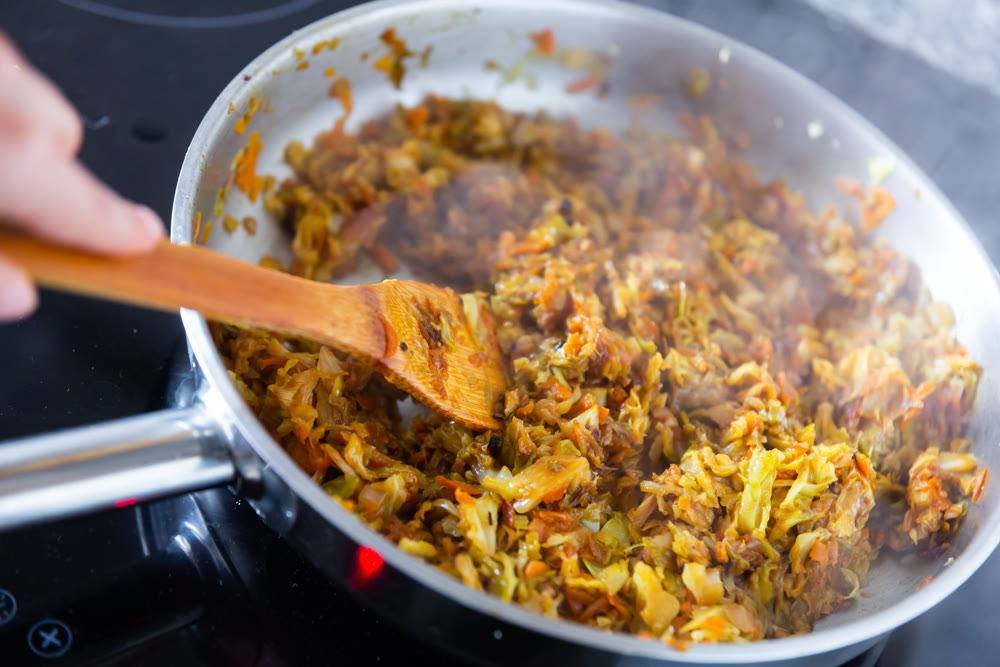 Hand stirring chopped cabbage in pan