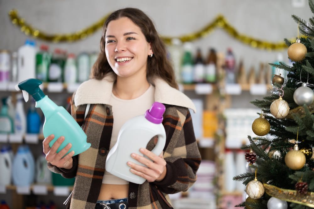 Young woman buyer chooses detergent and spray in decorated store
