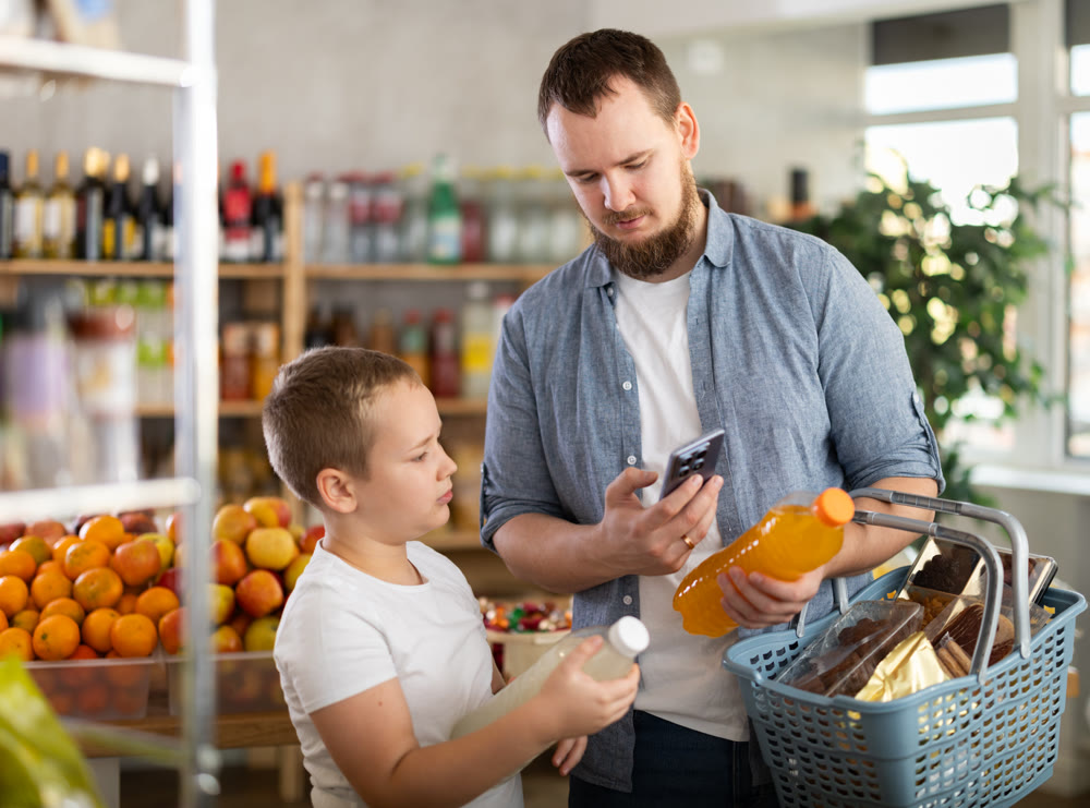 European man with son customer at shop scans QR code on drink bottle using phone camera