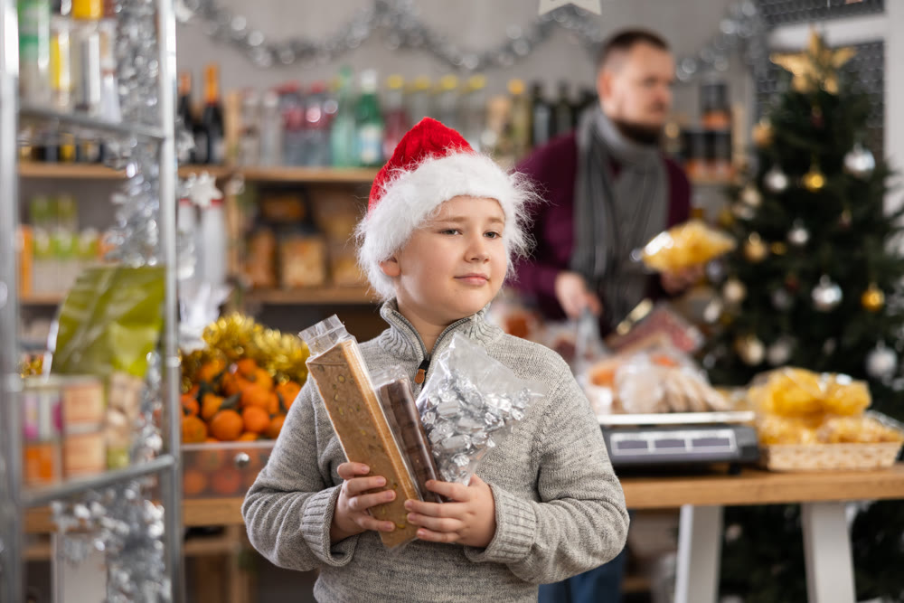 Little boy holding turrons and other sweets in market with Xmas decoration