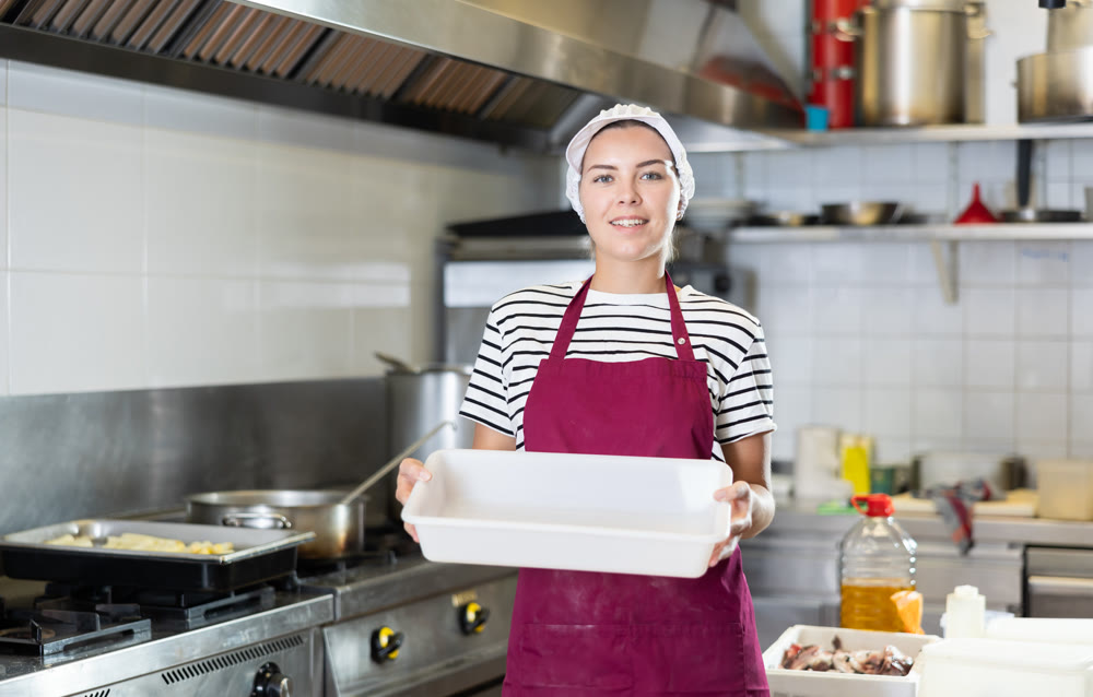 Smiling female worker with empty tray in professional kitchen setting