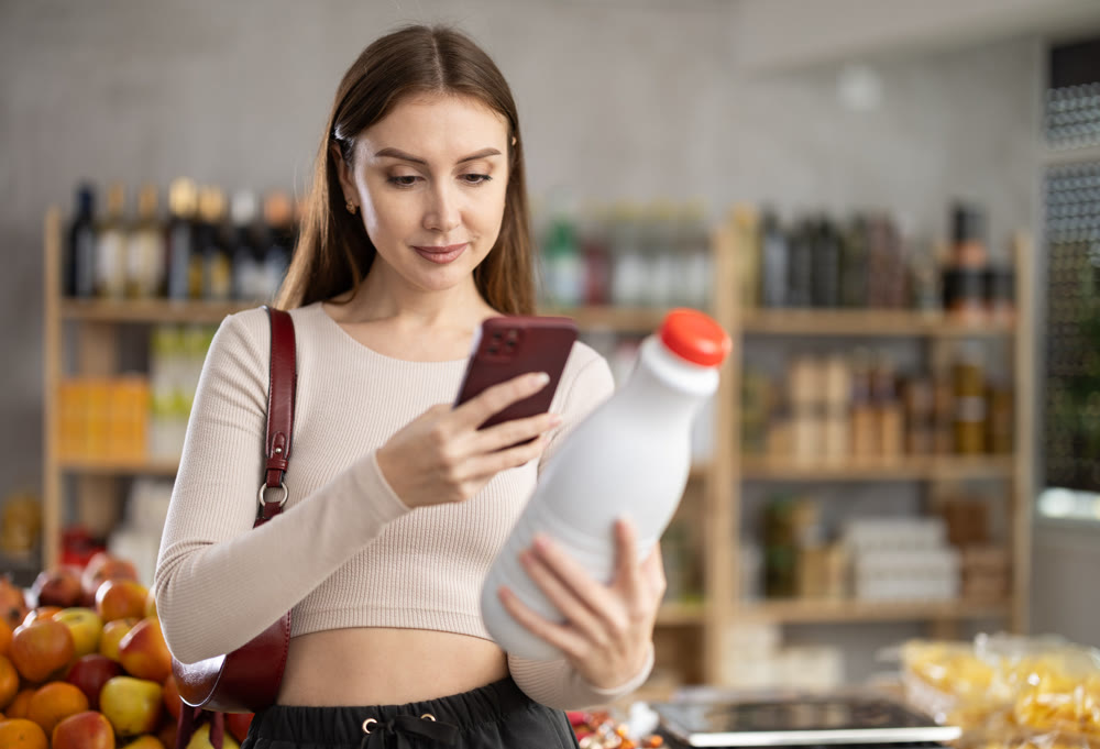 Female buyer checks suitability - scans QR code on bottle of milk label in grocery store