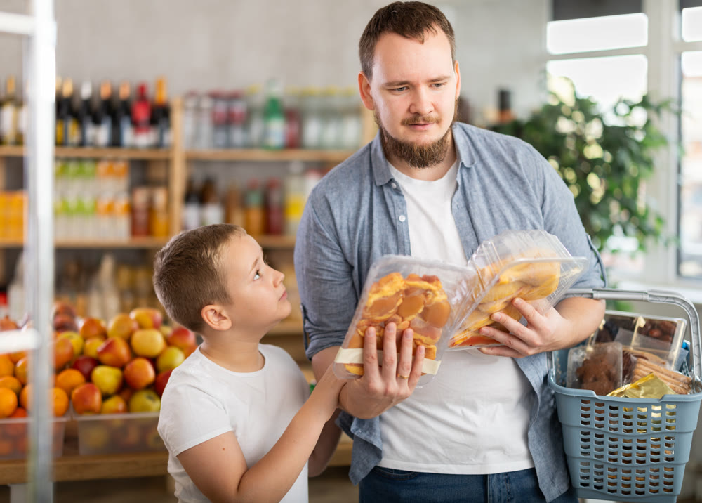 Father and preteen son choosing packaged cut poultry in grocery store