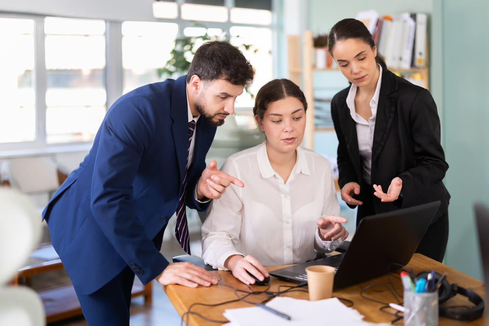 Man and woman help female colleague work with laptop