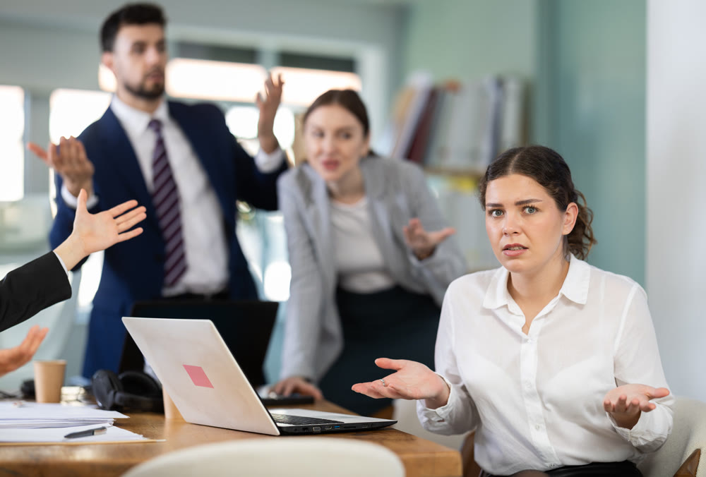 Group of people scolding sad colleague sitting at laptop in office