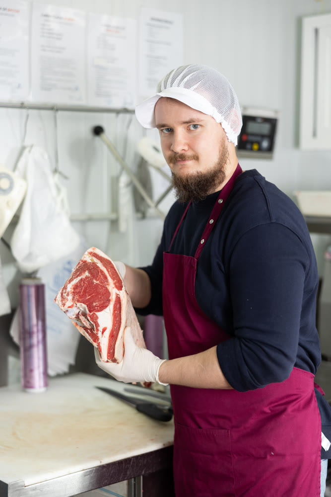 Butcher holding slab of beef rib steaks in shop processing room
