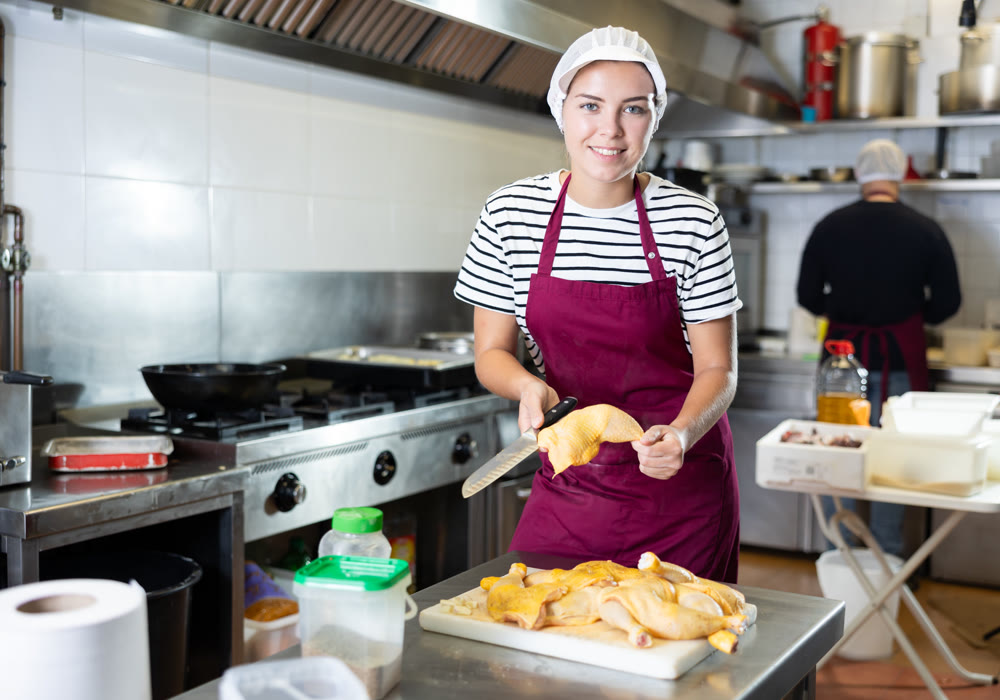 Girl cook prepares chicken legs - cuts them with knife before cooking