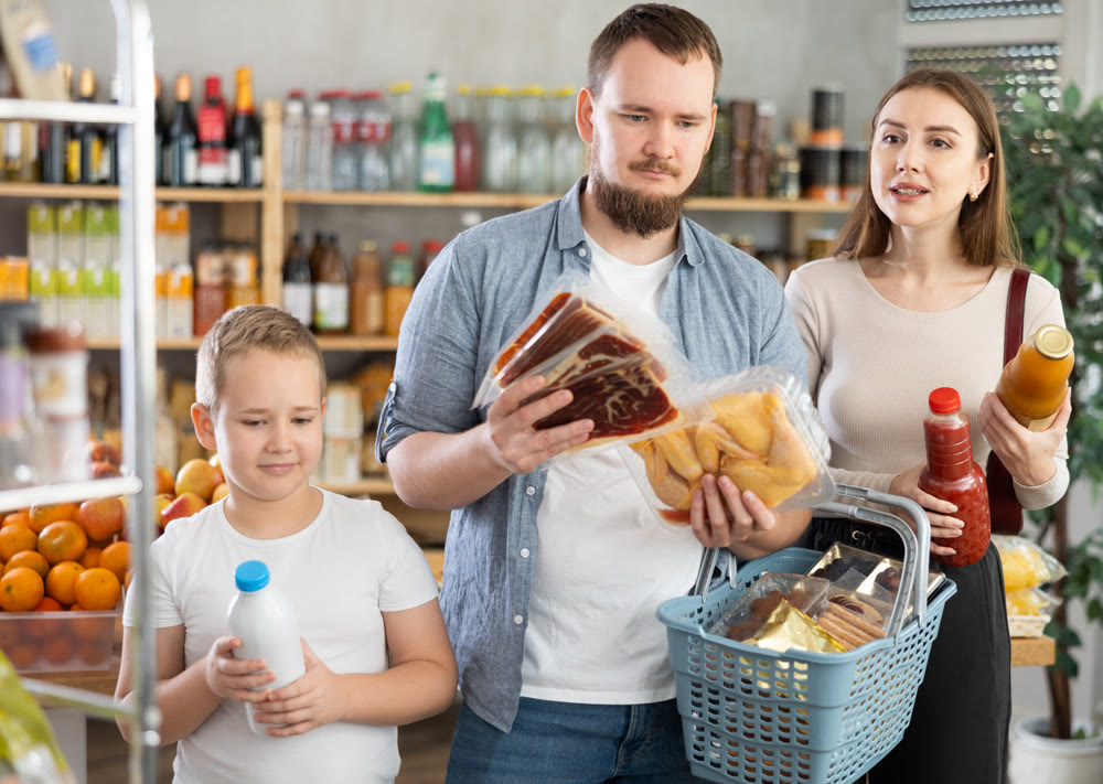 Young family with little son holding products in supermarket