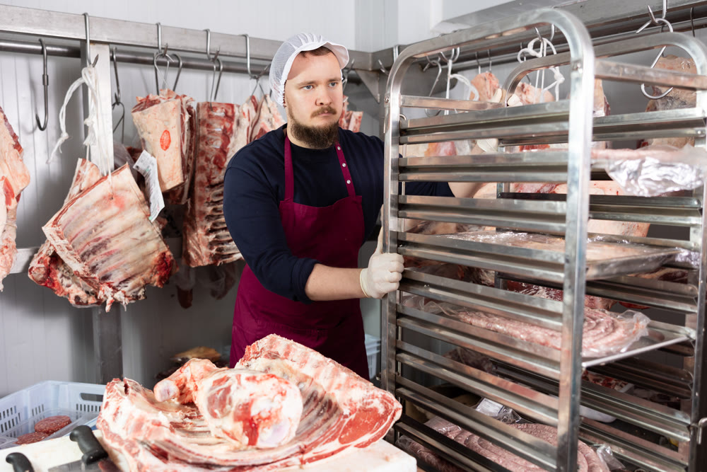 Portrait of male butcher while working in a butcher shop - moving trays with chopped carcasses