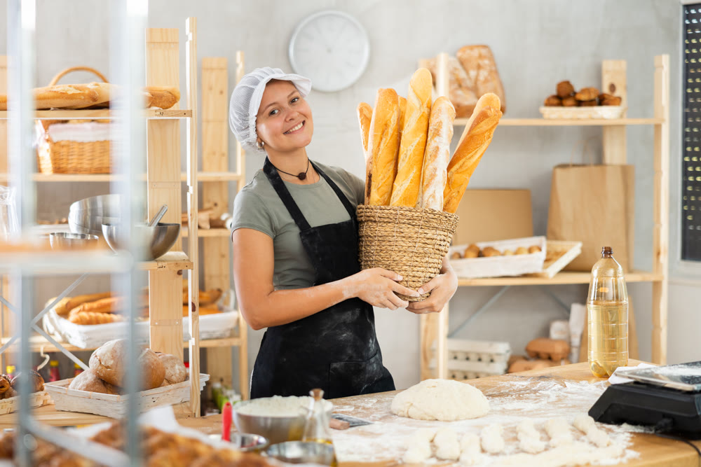 Young woman baker are standing near product range in bakery kitchen.