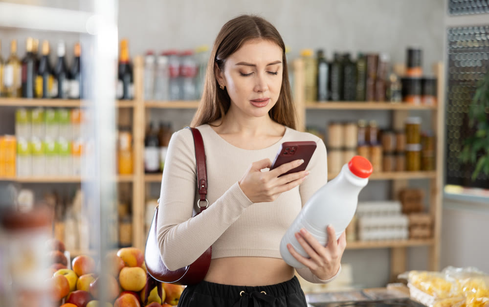 Female buyer checks suitability - scans QR code on bottle of milk label in grocery store