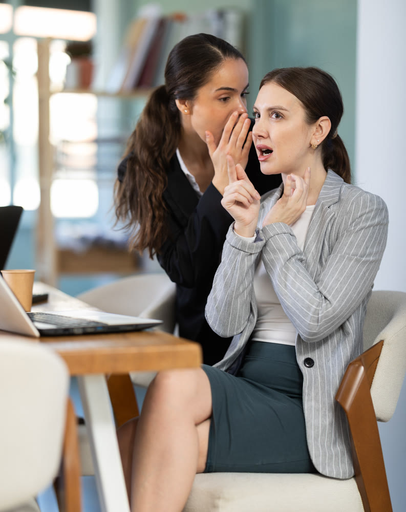 Female employee sharing gossip with surprised young colleague