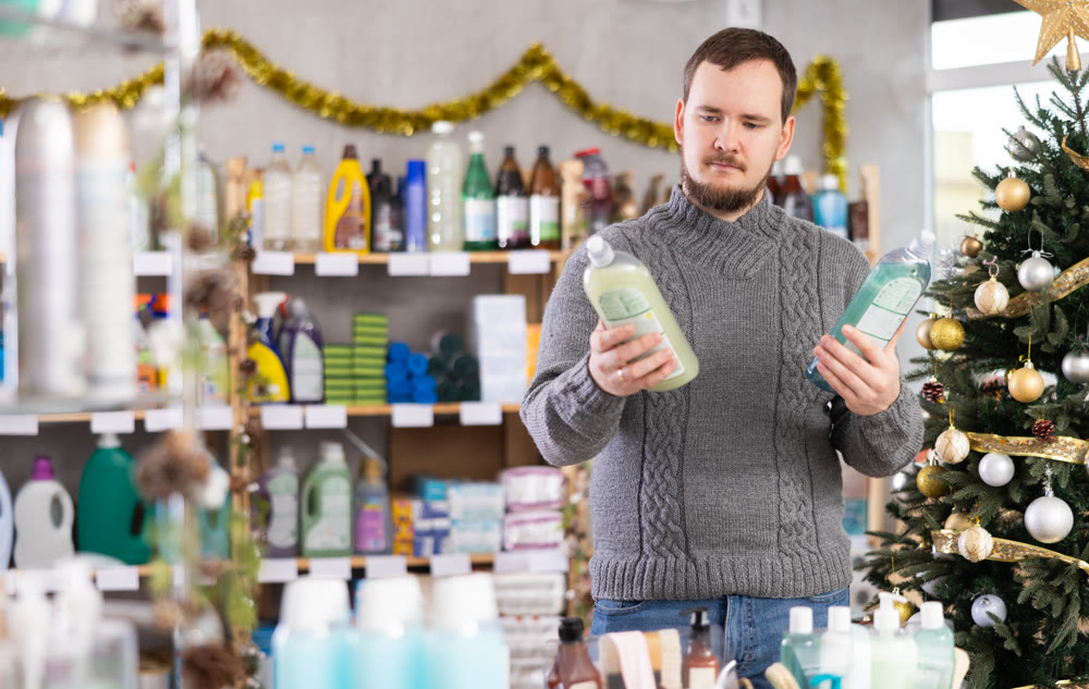 Middle-aged guy choosing dishwashing liquid in store with New Year decoration