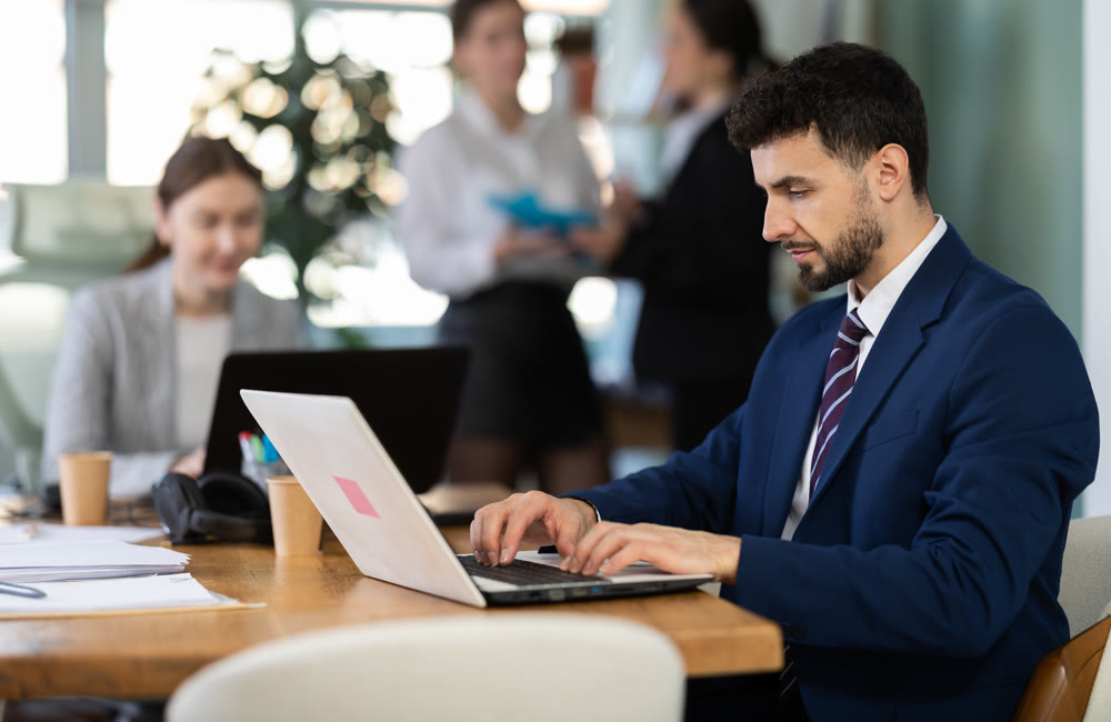 Young man works on laptop with colleagues
