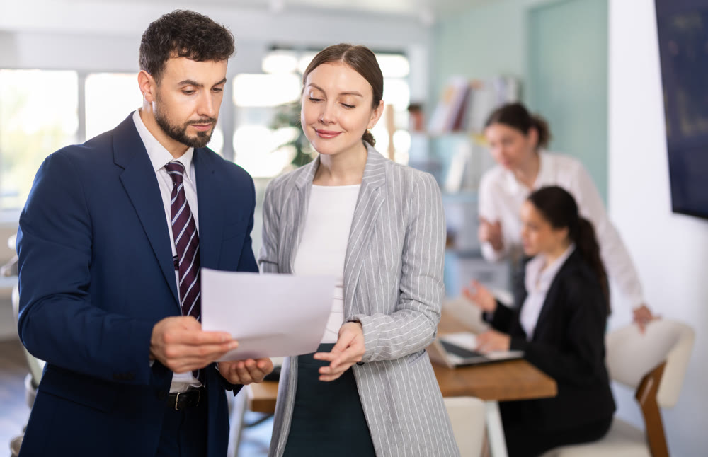 Male and female colleagues standing and reviewing paper documents in office