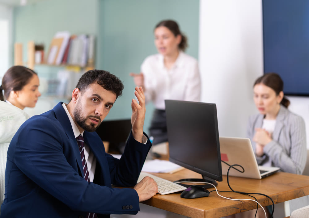 Young woman standing and scolding sad seated colleagues in office