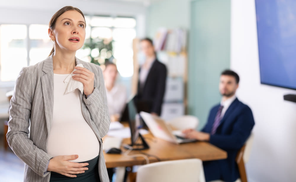 Distressed pregnant woman standing with sad expression in office