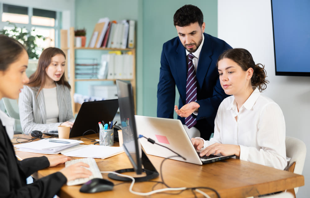 Young man helping female colleague work on laptop