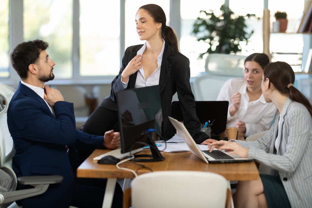 Flirtatious female employee sitting on table and talking to male colleague