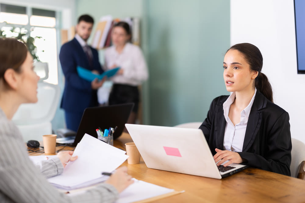 Young woman works on laptop with colleagues