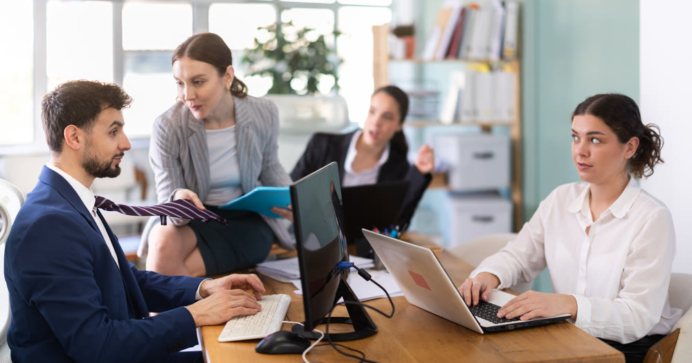 Young woman flirting with male colleague while sitting on office desk
