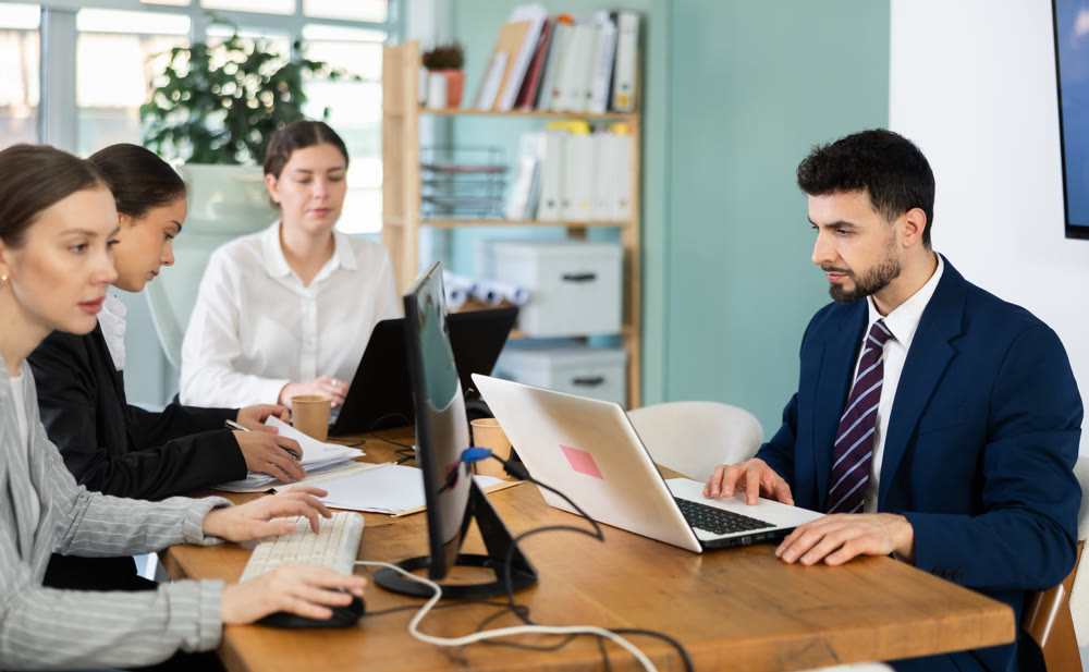 Young man works on laptop with colleagues