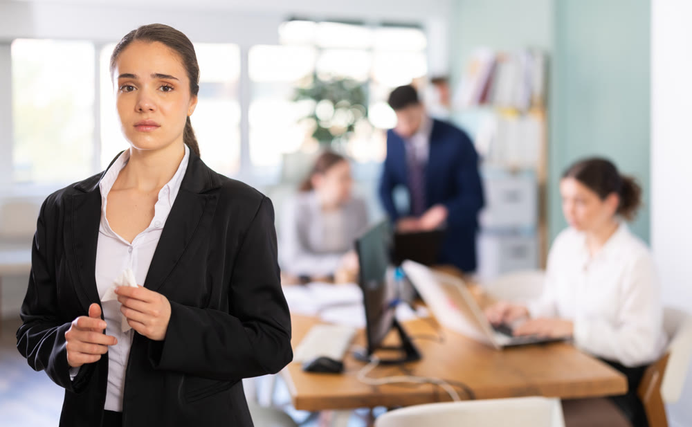 Distressed young woman standing with sad expression in office
